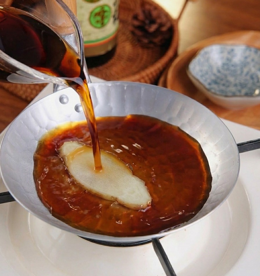 Un liquido scuro versato da una brocca in un pentolino argentato contenente una fetta di zenzero fresco.