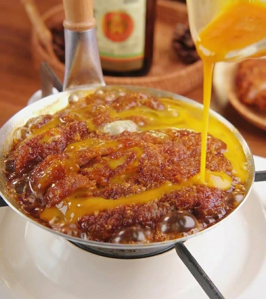 Uovo sbattuto versato da una ciotola sopra la cotoletta di maiale in una padella dargento.