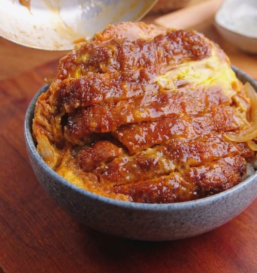 Una padella inclinata sopra una ciotola di riso per far scivolare la cotoletta con uova e cipolle.