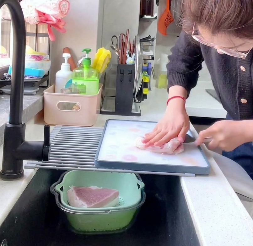 Vista laterale di una persona che usa una mannaia da cucina per tagliare il lombo di maiale crudo in fette di 1 cm su un tagliere.