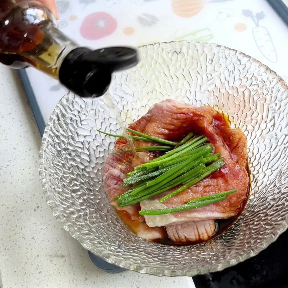 Una mano versa il condimento da una bottiglia in una ciotola con carne di maiale cruda, cipollotti verdi e amido bianco.