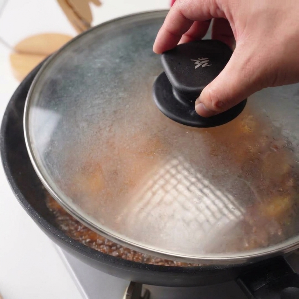 Mano che posiziona un coperchio di vetro trasparente sulla padella con il pollo in salsa.