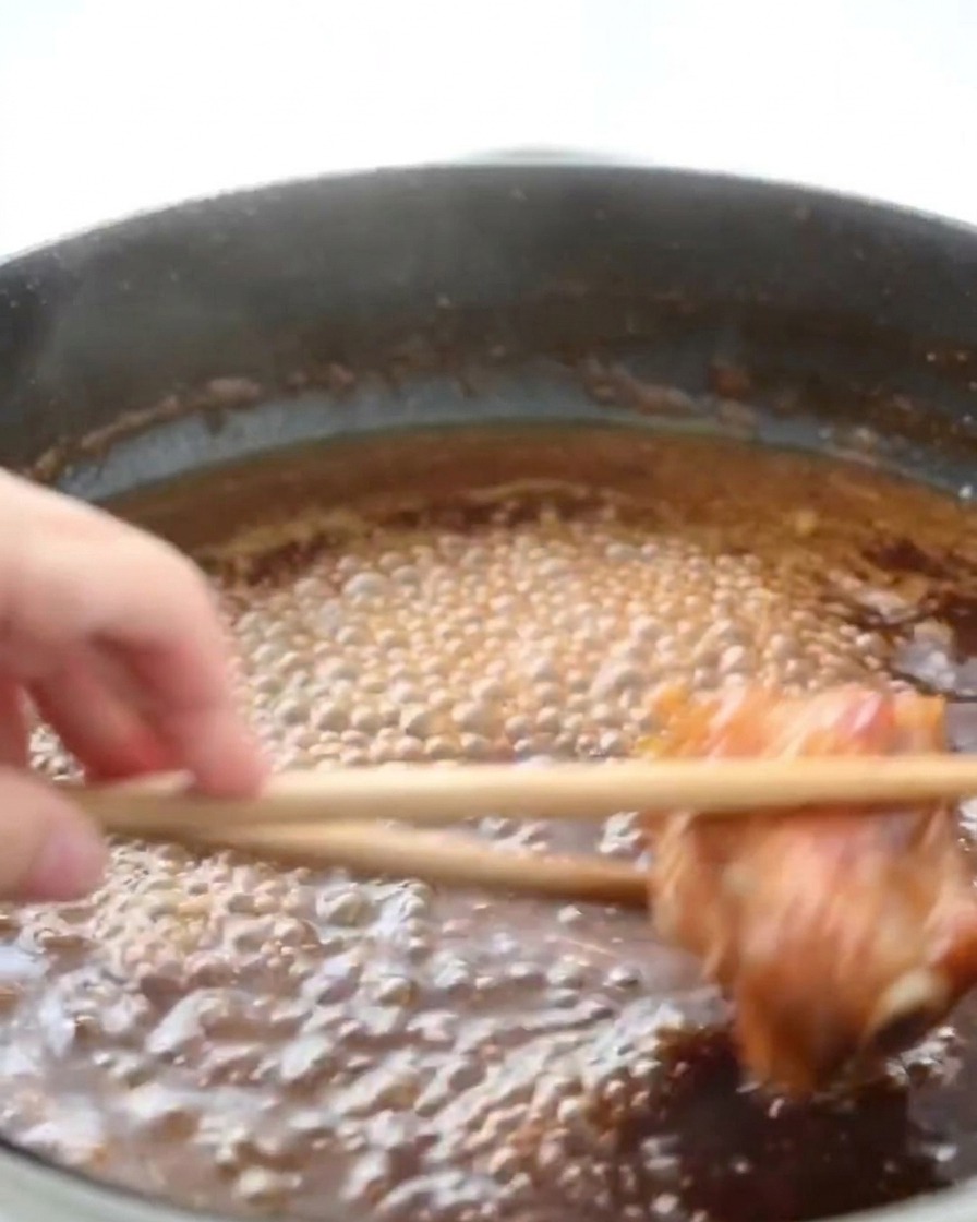 Sovracosce di pollo che sobbollono in una padella con salsa al miele scura e spumeggiante, con vapore che sale dalla superficie.