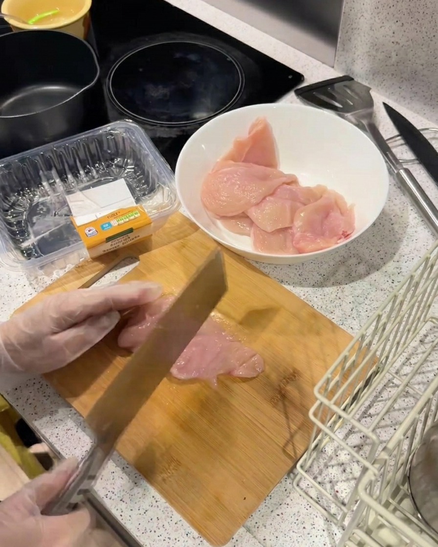 Il dorso di un coltello pesante viene usato per battere un filetto di pollo su un tagliere di legno per appiattirlo.