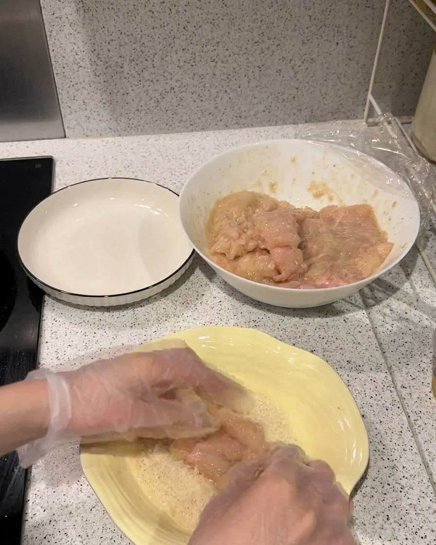Un filetto di pollo marinato viene premuto in un piatto giallo pieno di pangrattato Panko chiaro.
