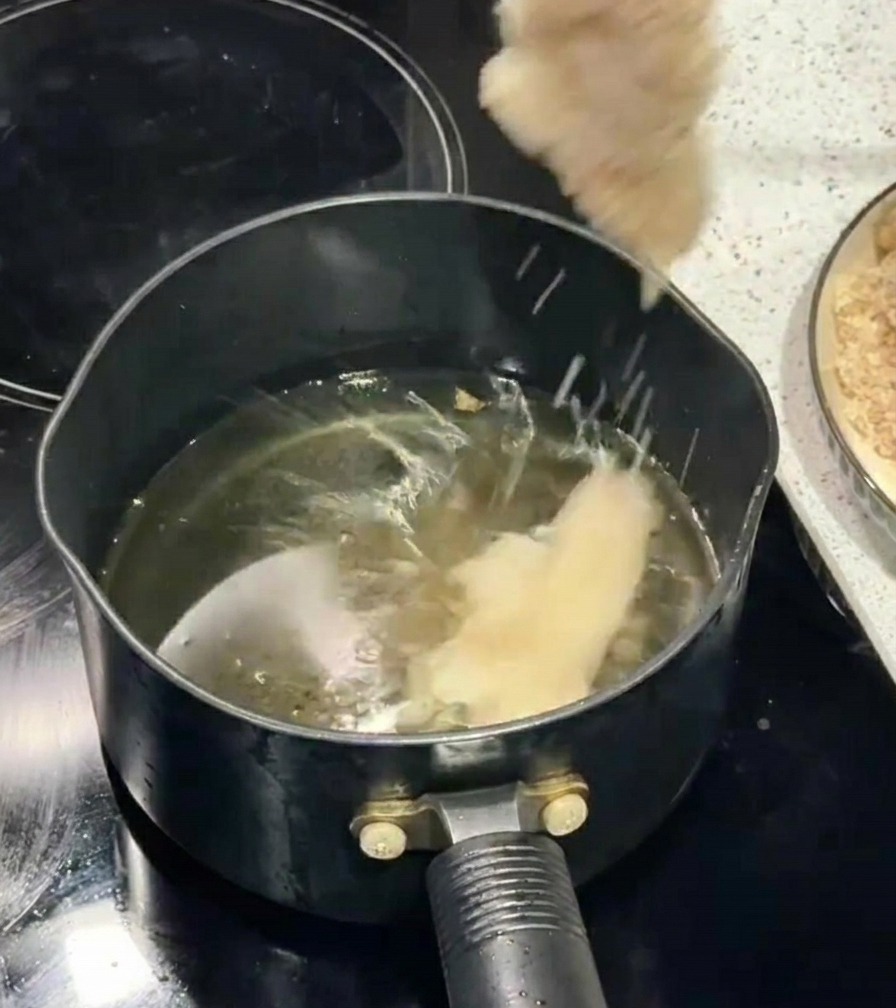 Una mano usa le bacchette per immergere un filetto di pollo impanato in una pentola di olio bollente.