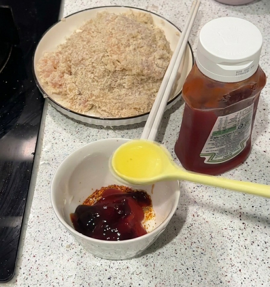 Un cucchiaio giallo versa olio bollente in una ciotolina bianca contenente ketchup e spezie.