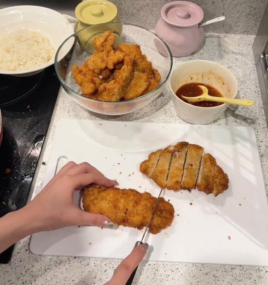 Una persona taglia una cotoletta di pollo fritta dorata a strisce su un tagliere di plastica bianca.