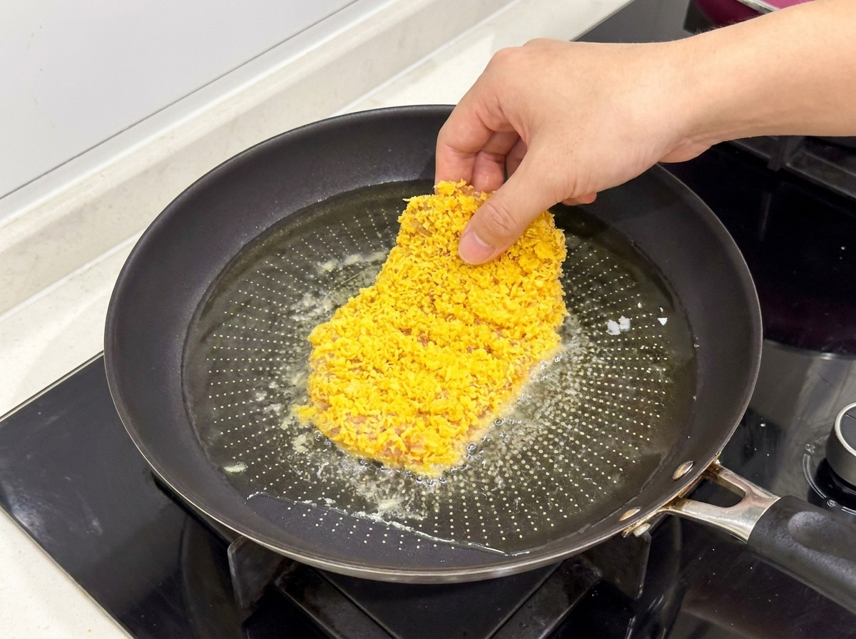 Una cotoletta di pollo impanata mentre viene immersa in una padella con olio bollente e scintillante.