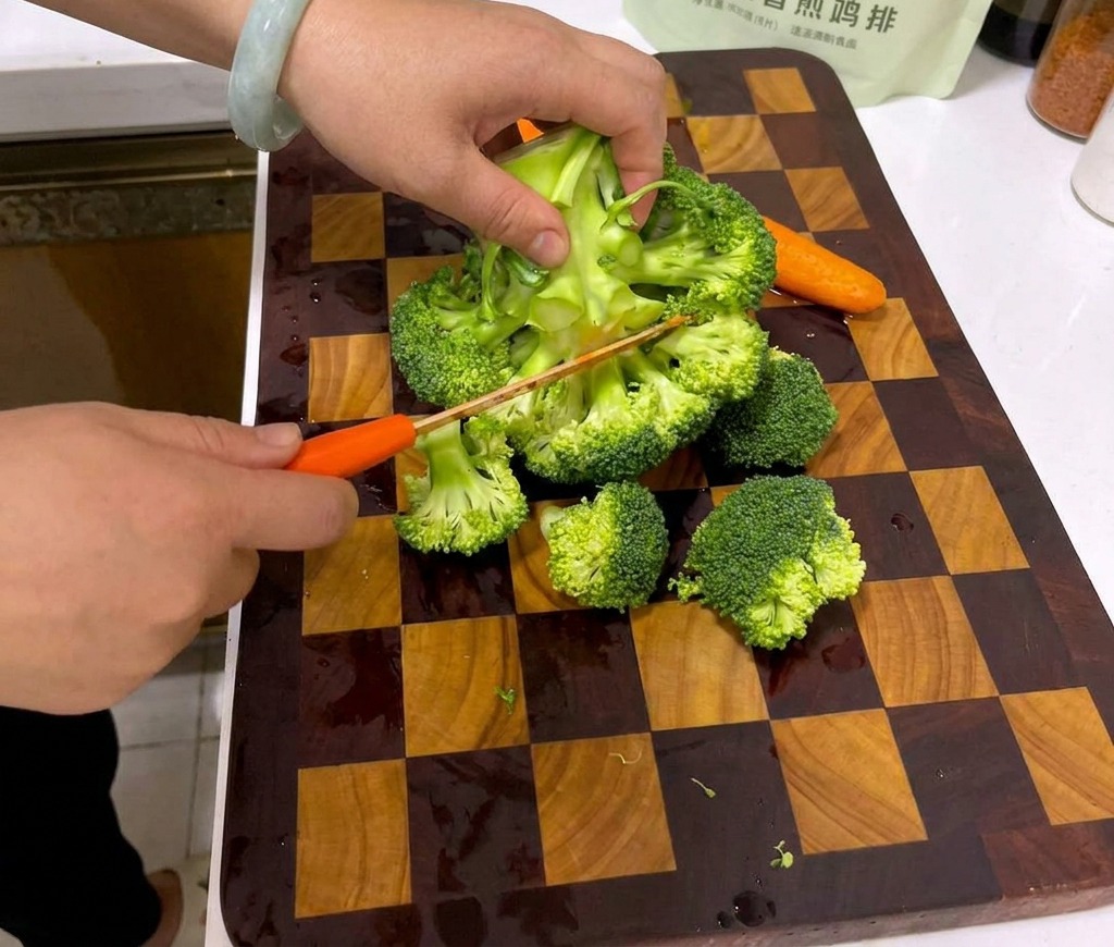 Mani che tagliano una testa di broccolo in piccole cime su un tagliere di legno a scacchi.