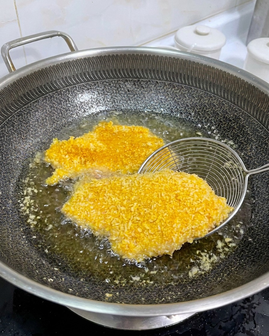 Un colino in metallo che solleva una cotoletta di pollo dorata in una padella per mostrare il lato cotto.