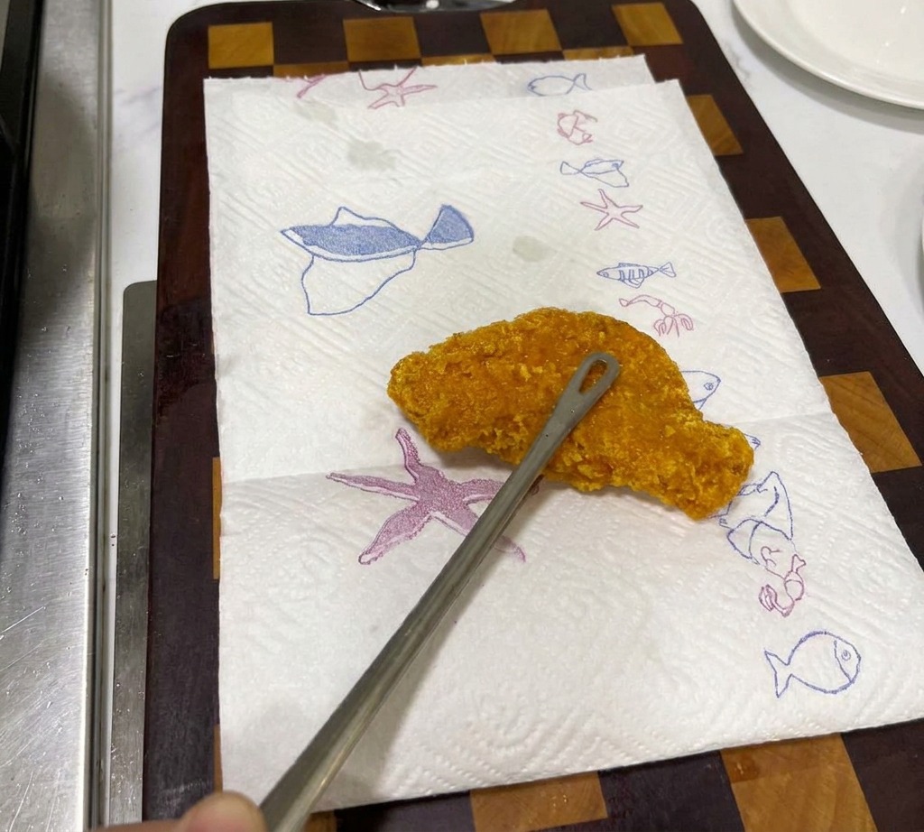 Una cotoletta di pollo fritto dorata e croccante che riposa su carta assorbente per eliminare lolio.