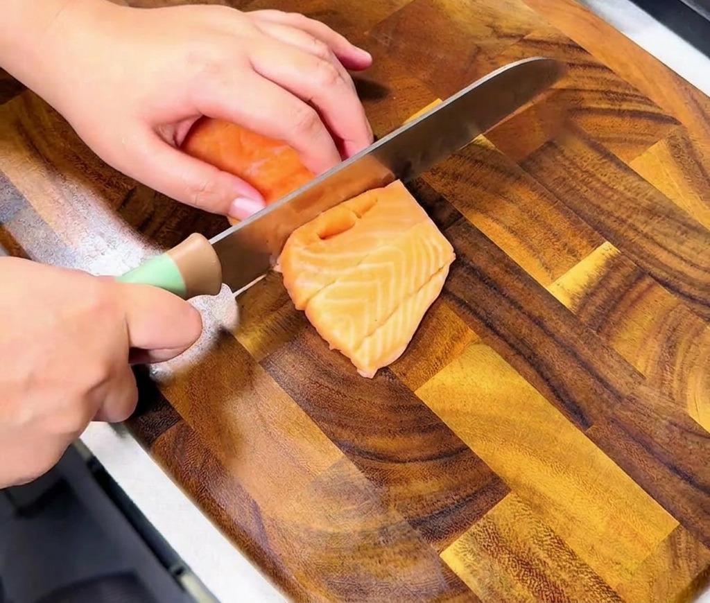 Mani che affettano un filetto di salmone fresco per creare cubetti uniformi su un tagliere.