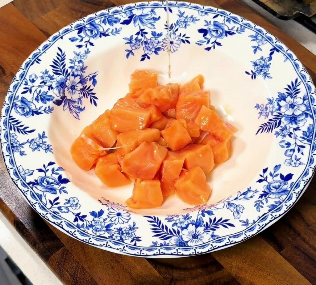 Salsa di soia e mirin versati sopra i cubetti di salmone crudo in una ciotola di ceramica decorata.