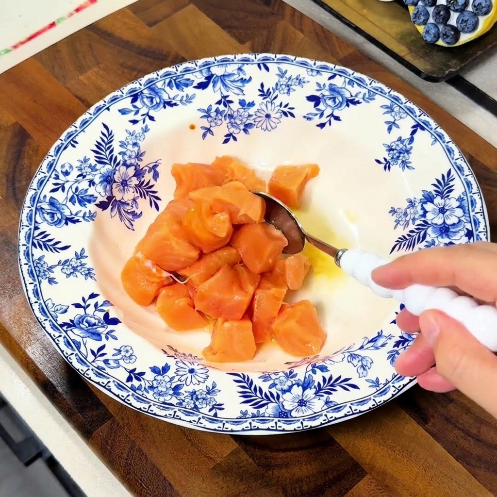 Un cucchiaio che mescola i cubetti di salmone in una ciotola per coprirli bene con il liquido della marinatura.