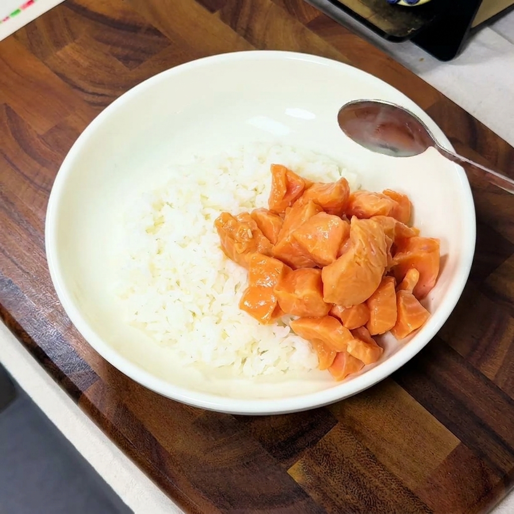 Cubetti di salmone marinato adagiati su un lato di una ciotola bianca colma di riso bianco.