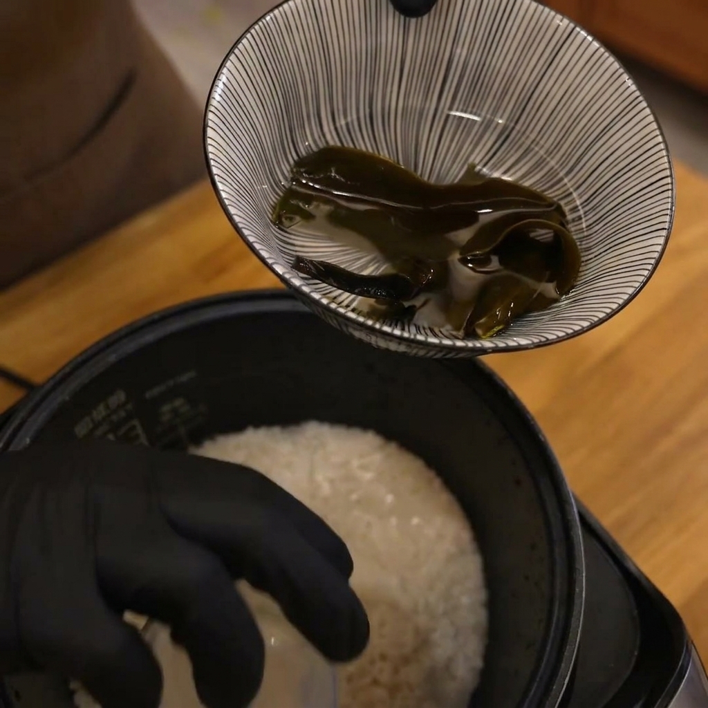 Una mano guantata che tiene un misurino sopra una pentola di riso crudo.