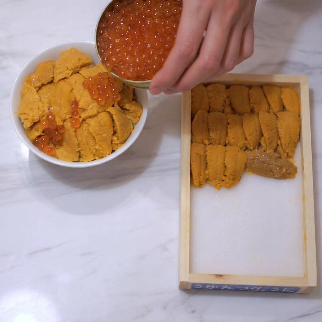 Uova di salmone rosso-arancio versate da una piccola scatola dorata su una ciotola guarnita con ricci di mare.