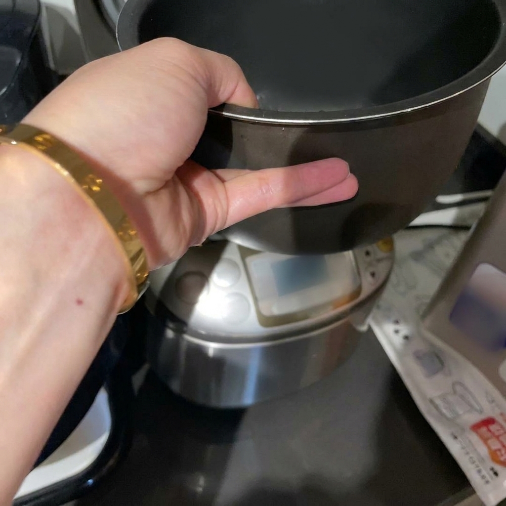 Una mano che regge il contenitore interno scuro di un cuociriso con riso bianco crudo immerso nellacqua.