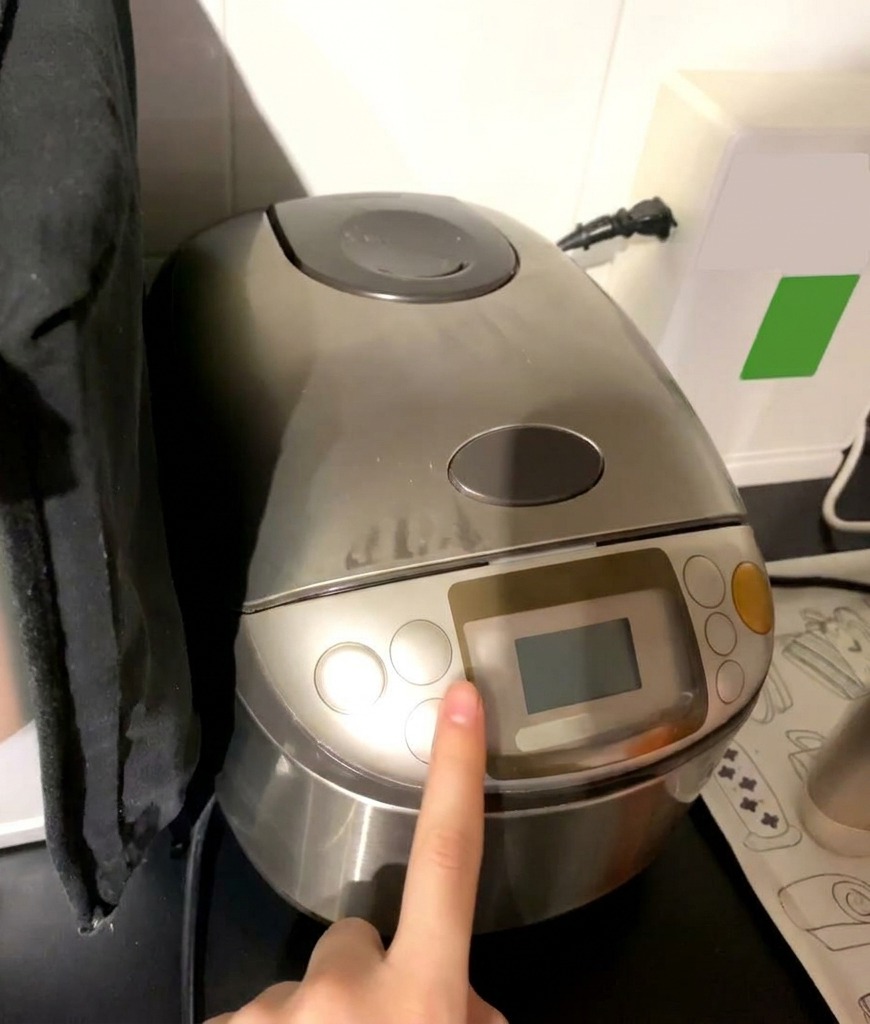 Un dito che preme il tasto di avvio su un cuociriso Zojirushi argento con display digitale visibile.
