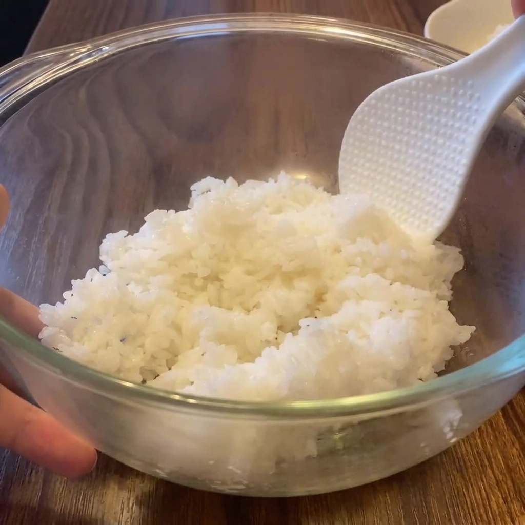 Una spatola per riso bianca che sgrana il riso bianco bollente e fumante dentro una ciotola di vetro.