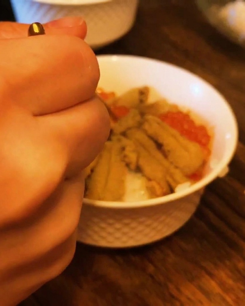 Primo piano di una mano che usa un cucchiaino per riempire gli spazi tra i ricci di mare con uova di salmone arancioni.