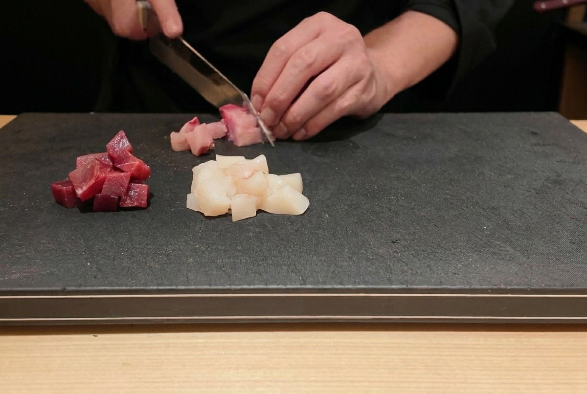 Uno chef che taglia tonno e ricciola freschi a cubetti su un tagliere nero.