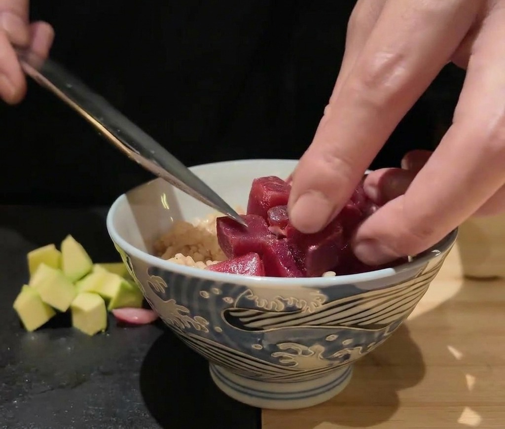 Cubetti di pesce crudo e capesante posizionati con cura su una ciotola di riso aiutandosi con la lama di un coltello.