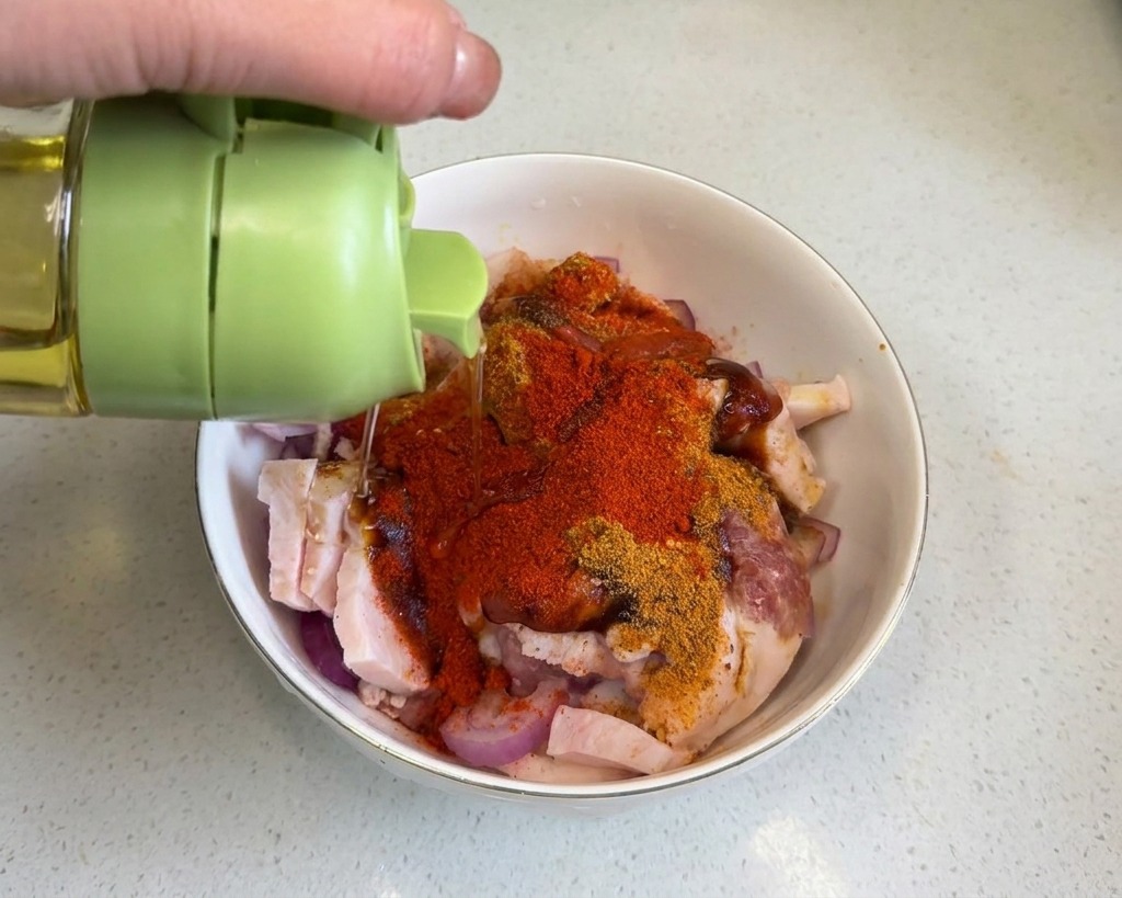 Olio di semi versato da un contenitore con tappo verde sulla pancetta ricoperta di spezie rosse.