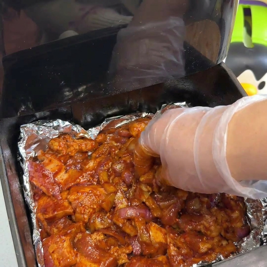 Una mano che stende uno strato spesso di maiale marinato e cipolle in un cestello della friggitrice ad aria.