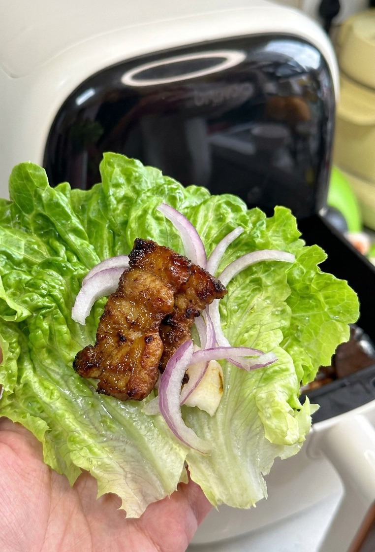 Una foglia di lattuga tenuta in mano, contenente aglio, cipolla e un pezzo di pancetta arrostita lucida e dorata.