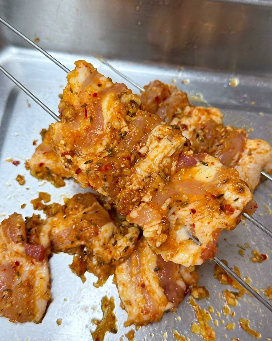 Fette di pancetta marinata infilzate su due sottili spiedini di metallo sopra un vassoio.