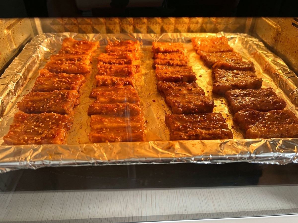 Fette di pancetta marinata che cuociono su una teglia nel forno illuminato.