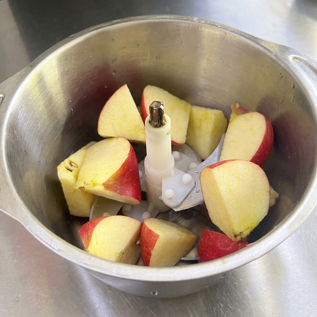 Un frullatore in acciaio inossidabile riempito con pezzi di mela rossa, pera e cipolla bianca.