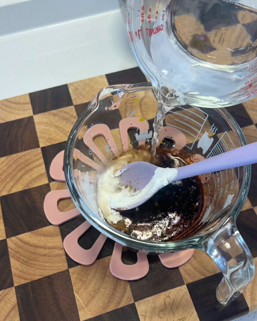 Acqua versata da un contenitore di vetro in una tazza con un mix scuro di salsa di soia e spezie.