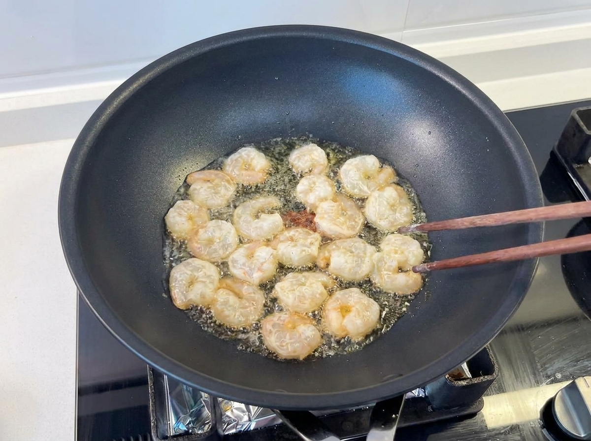 Gamberi saltati con bacchette di legno in un wok nero con olio bollente.