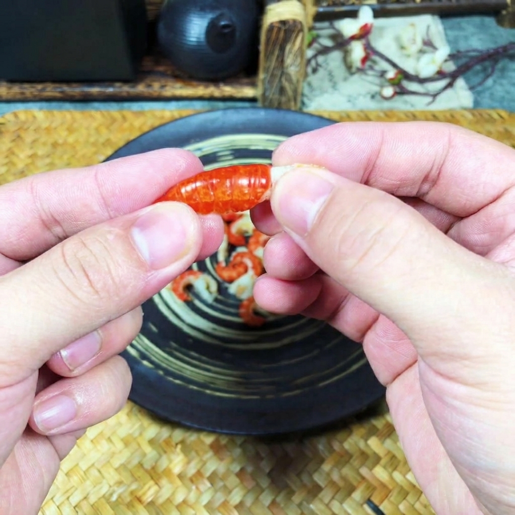 Primo piano di mani che rimuovono il guscio arancione da una coda di gambero cotta.