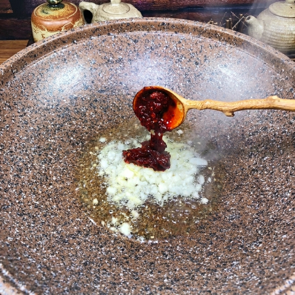 Un cucchiaio di legno aggiunge la pasta di peperoncino rosso scuro nel wok con gli aromi.