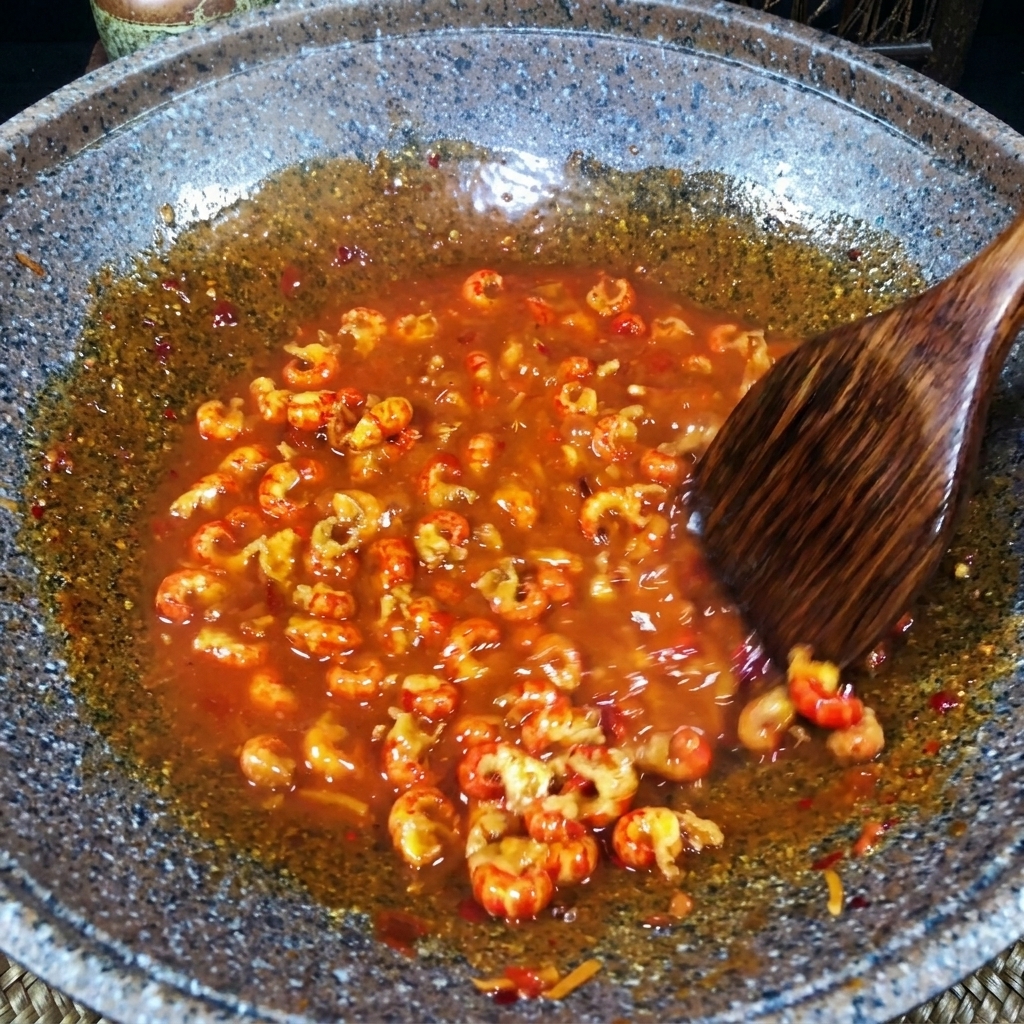 Una spatola di legno mescola i gamberi in una densa salsa rossa in padella.