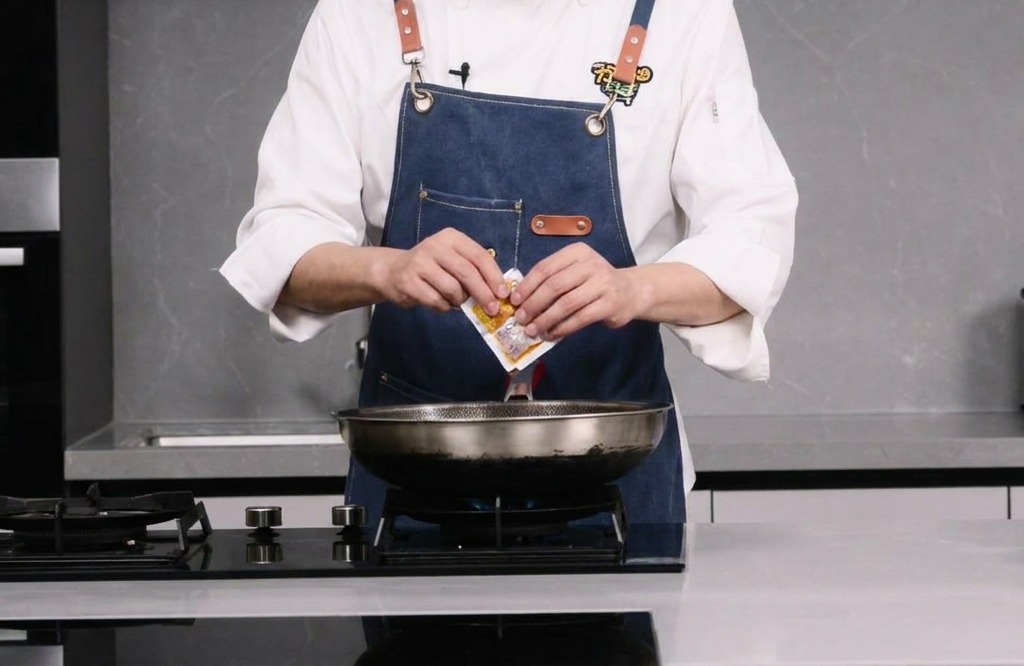 Una persona apre una piccola confezione di base piccante per hot pot sopra un wok.