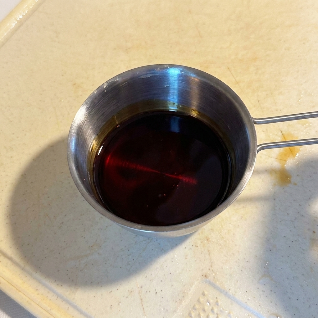 Una miscela di salsa scura e lucida in un piccolo contenitore graduato di acciaio.