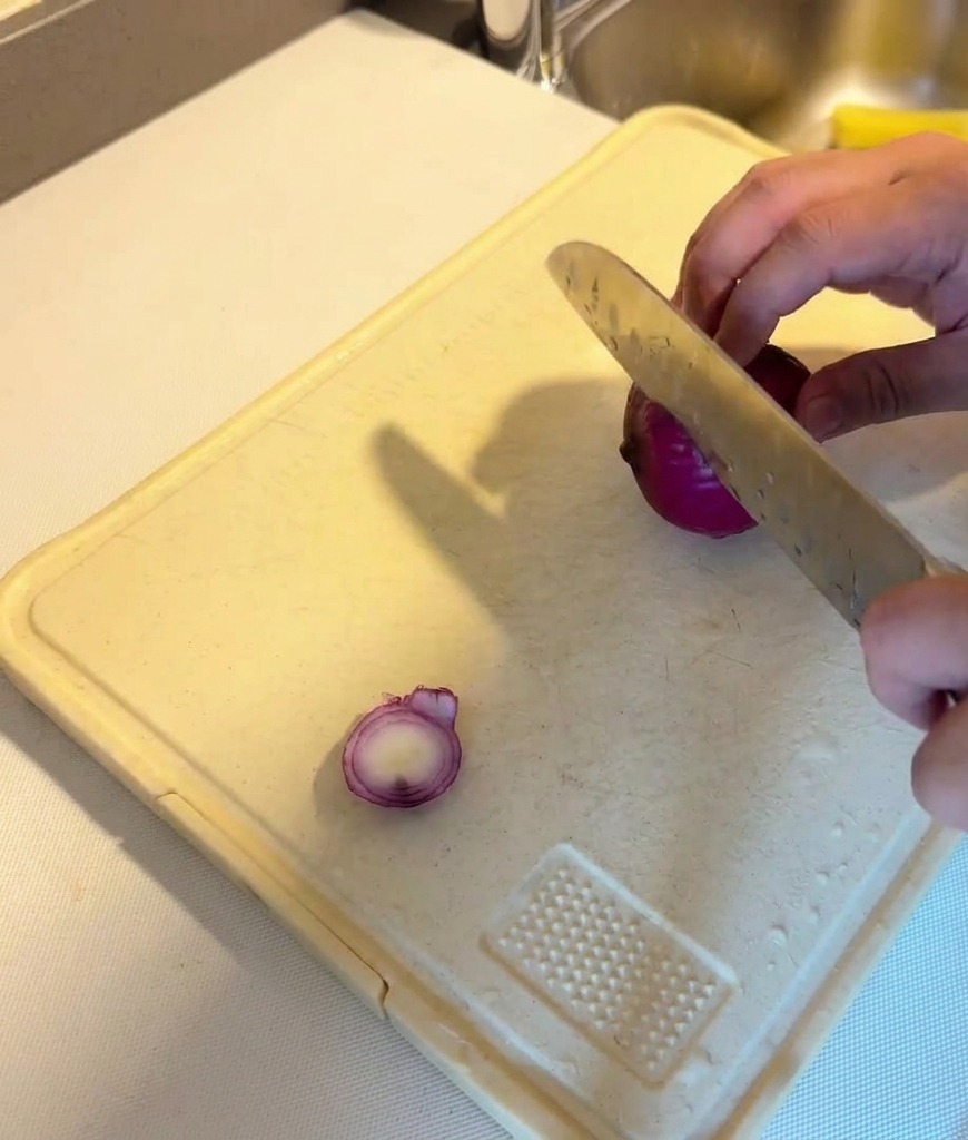 Affettatura di una cipolla rossa a rondelle sottili su un tagliere di plastica bianco.
