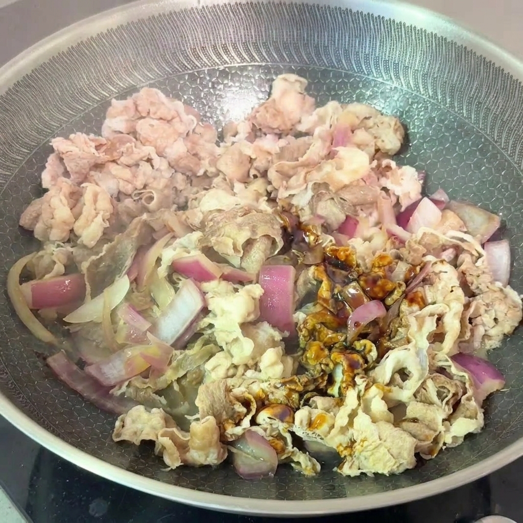 Fette di manzo sbollentate e cipolle rosse saltate con una salsa scura a base di soia in padella.