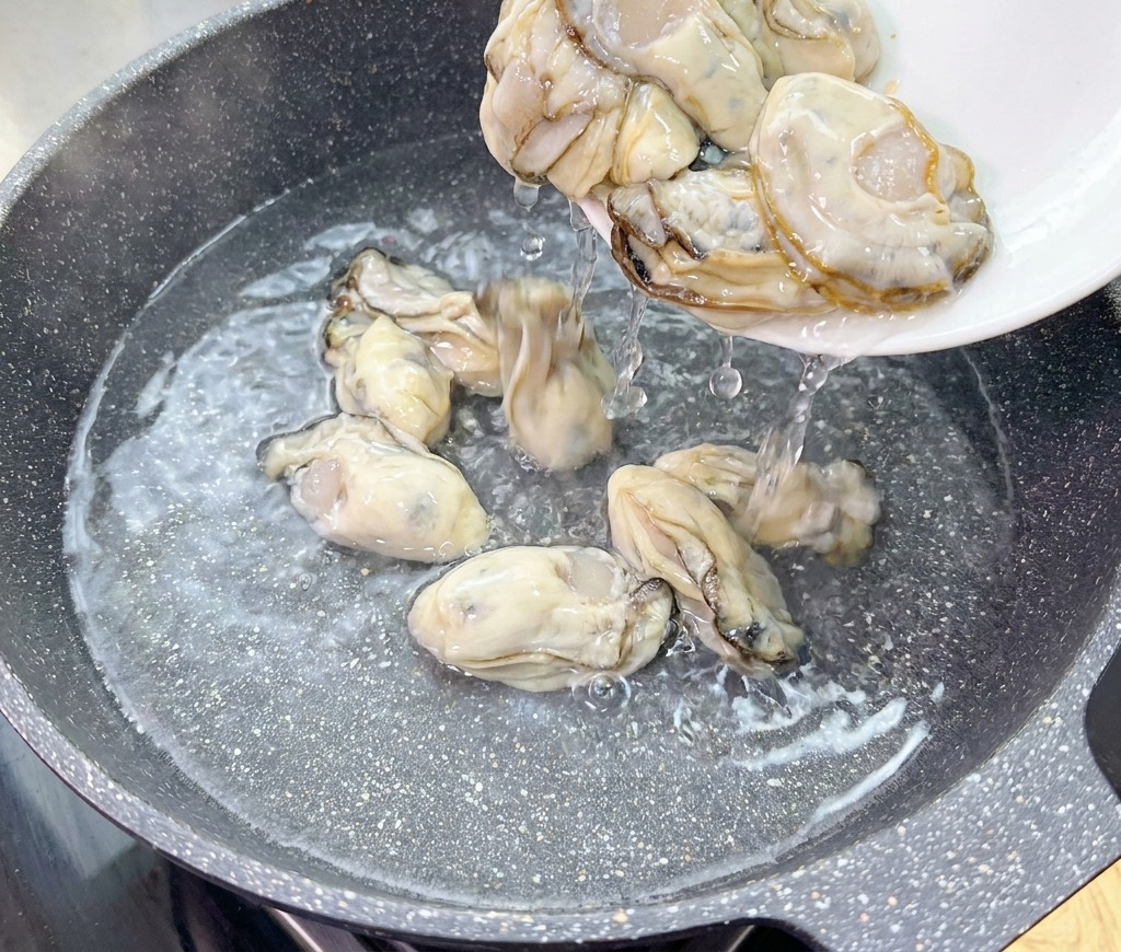Ostriche fresche e crude scivolano da un piatto bianco in un wok con acqua fredda salata.