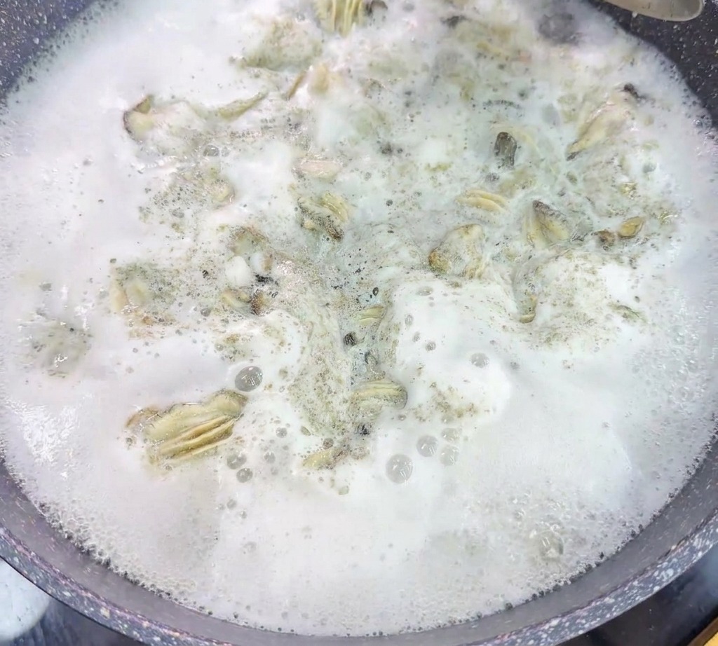 Un colino metallico solleva le ostriche da una pentola dacqua bollente e molto schiumosa.