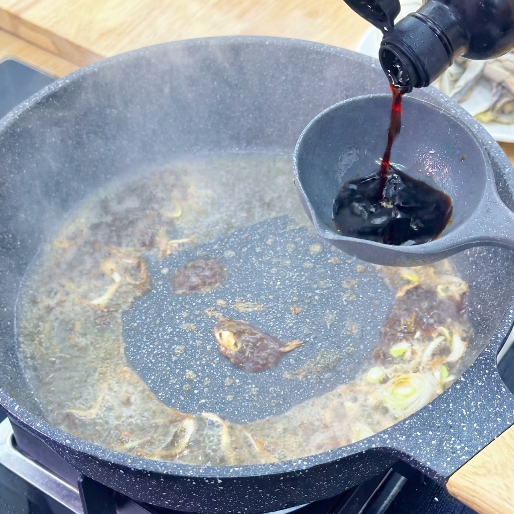 Salsa di soia chiara versata da una bottiglia scura in un mestolo sopra la salsa che sobbolle.