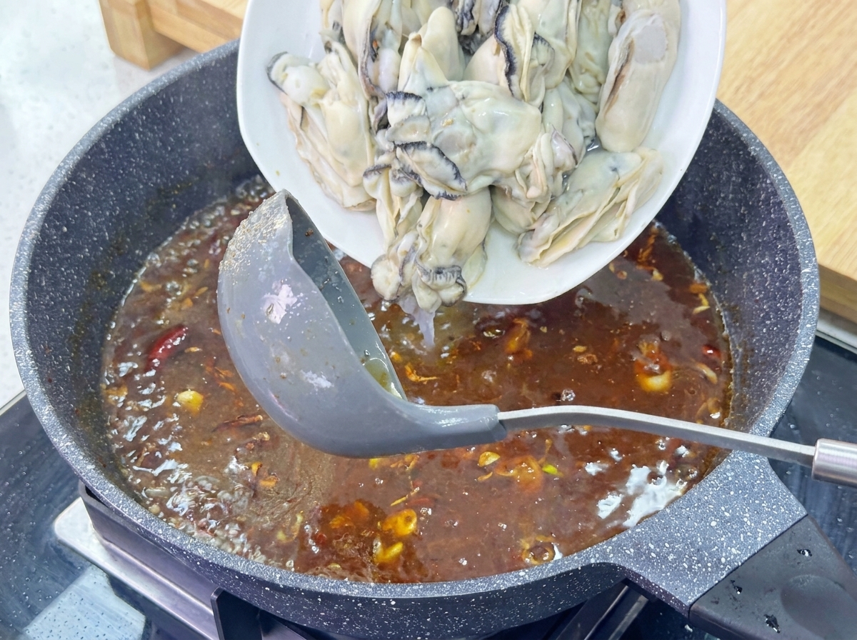 Un piatto di ostriche sbollentate scivola in una salsa bruna ribollente in una padella scura.