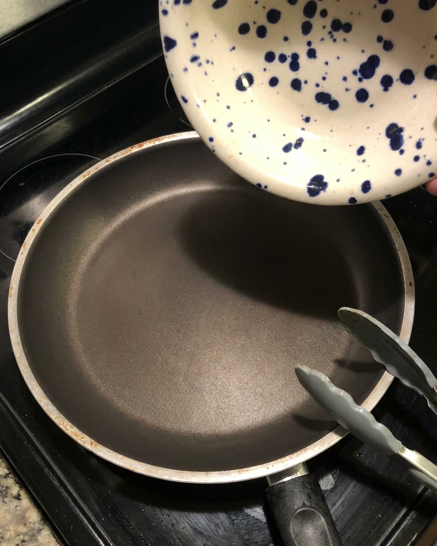 Una ciotola di ceramica a macchie blu versa del liquido scuro di marinatura in una padella vuota e calda per creare una riduzione di salsa.