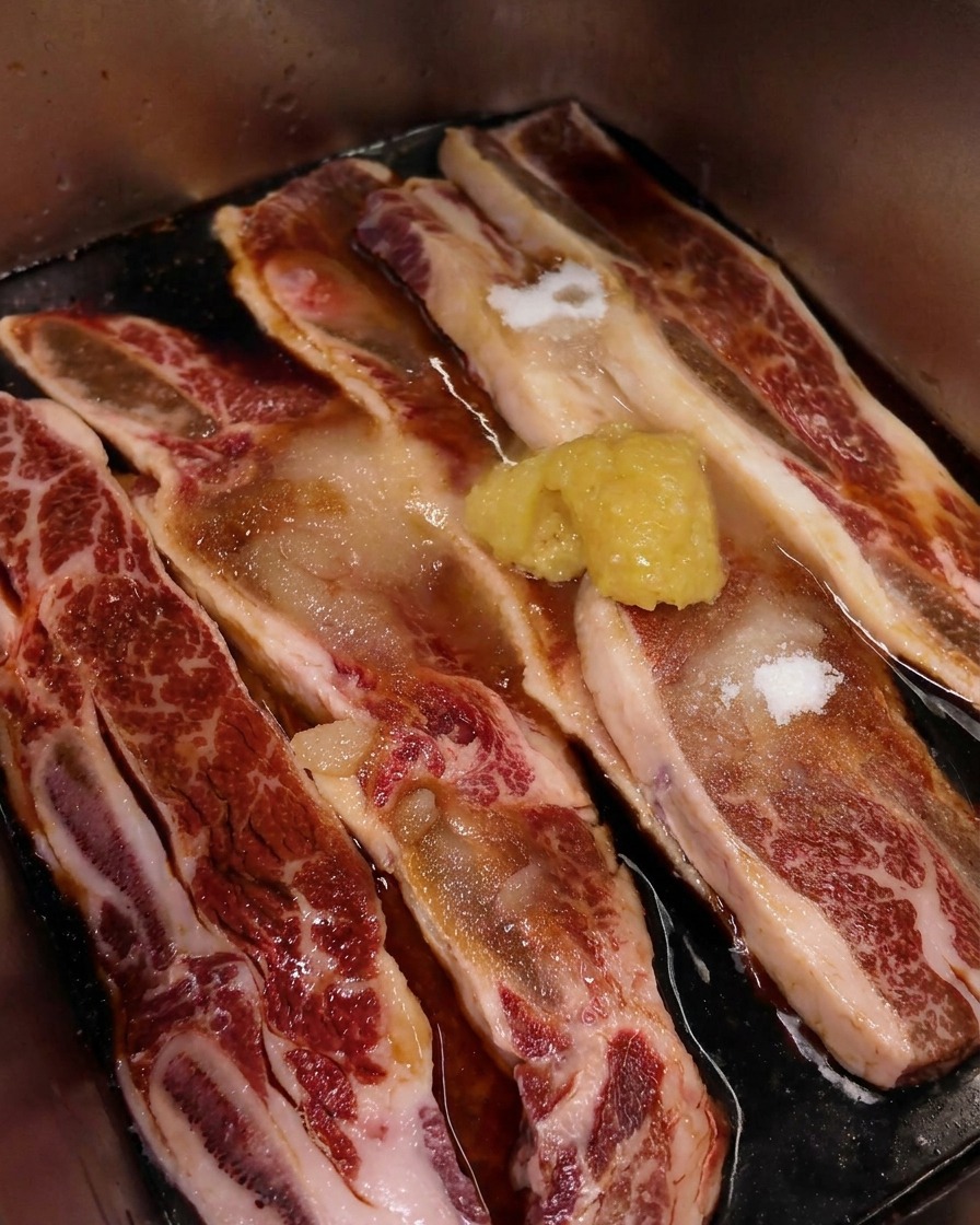 Dettaglio di un mucchietto di aglio tritato sopra costine di manzo venate di grasso in marinata scura.