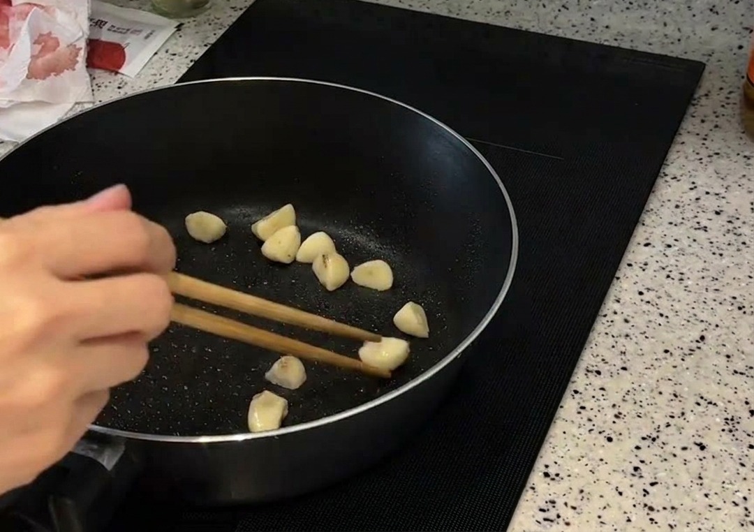 Una manciata di spicchi daglio interi mescolati con bacchette di legno in una padella scura mentre diventano dorati.